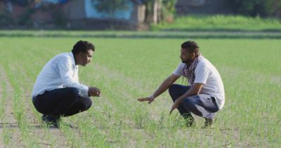 two men kneeling and talking in field