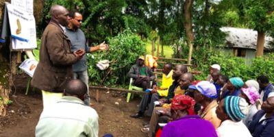 Two tall men talking to a group of African farmers in a field.