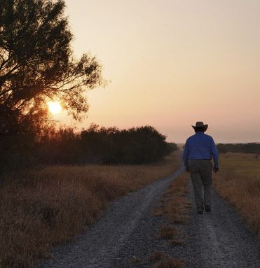 Man walking away down a dirt road at sunset with orange sky