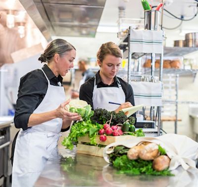 Two women in restaurant kitchen sorting vegetables