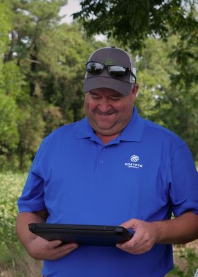 Man wearing Corteva shirt looking at laptop in field