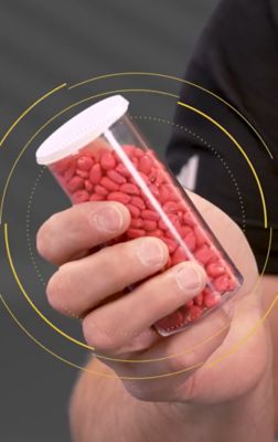 close up of man's hand holding bottle of red-colored seeds