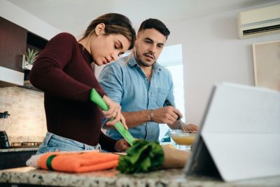 man and woman cooking with recipe displayed on a tablet on the counter