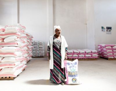 Woman standing next to a seed bag, among pallets of seed bags