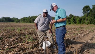 two men in field viewing data on phone