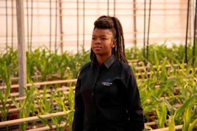 Woman wearing Corteva shirt walking in aisle in a greenhouse