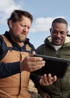 two men in field viewing data on tablet