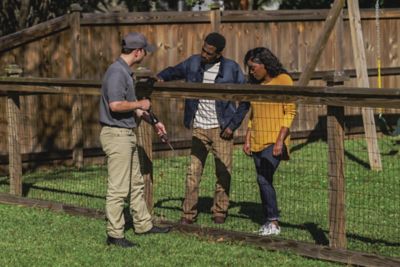 Certified Sentricon Specialist speaks to a male and female homeowner along a wooden fence line