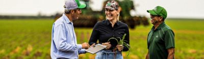 Homem com um tablet na lavoura de milho mostrando para uma mulher e outro homem.