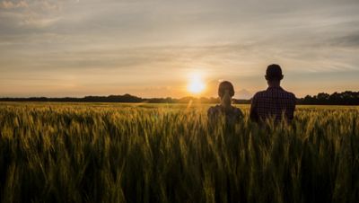 man and woman standing in wheat field and staring at the sunset