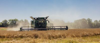 Platform header driving through a field in a cloud of dust.