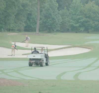 A golf hole with superintendents working to blow out grass in the sand traps