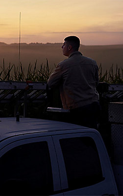 Man by truck looking over field at sunset