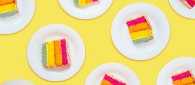 Multiple plates with a piece of cake on each plate. The cake has a blue layer, yellow layer, orange layer and pink layer.
