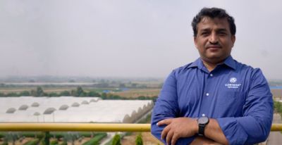 Photo of Corteva research scientist Ramu Punna standing on a rooftop with fields and multiple greenhouse enclosures in the distance. Photo taken at Corteva's research center in Hyderbad, India.