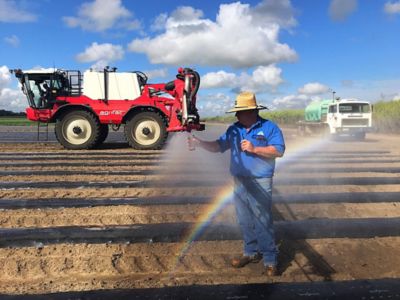 Man in a ploughed field with farm equipment & a small rainbow