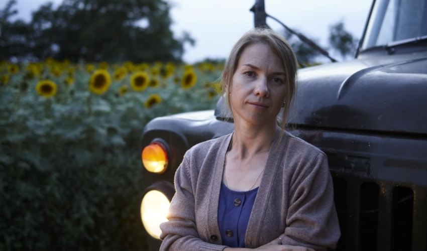 Woman standing infront of a truck parking infront of a field of sunflowers