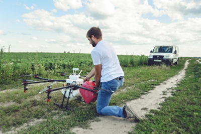 Man kneeling next to drone on grassy dirt road