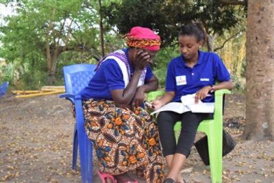 woman farmer with USAID staff seated outdoors reviewing paperwork