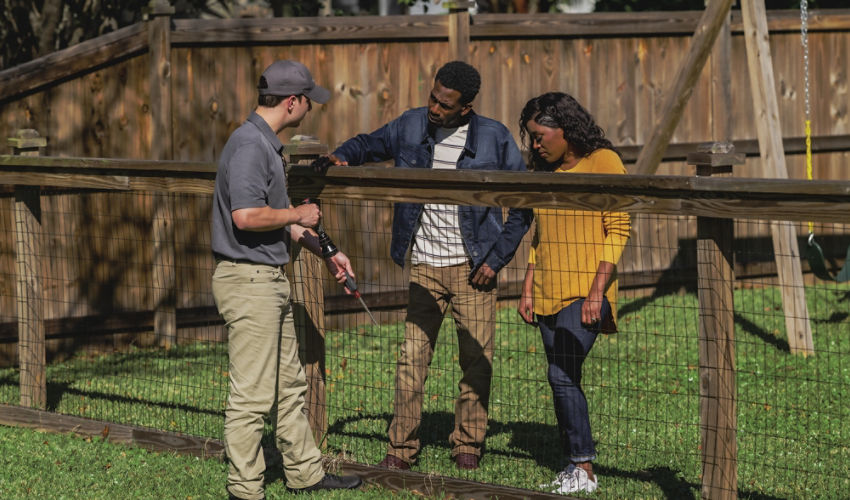Certified Sentricon Specialist speaks to a male and female homeowner along a wooden fence line