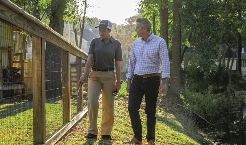 Certified Sentricon Specialist speaks with malle homeowner while walking along fence line.