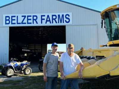 Jacob Belzer and his grandfather Gary Belzer standing next to a tractor