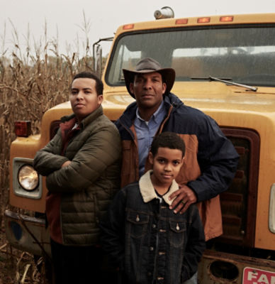 Man and two sons standing in front of truck in cornfield