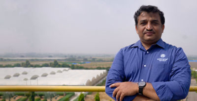 Photo of Corteva research scientist Ramu Punna standing on a rooftop with fields and multiple greenhouse enclosures in the distance. Photo taken at Corteva's research center in Hyderbad, India.