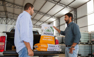 Dois homens conversando com sacarias de milho no bagageiro de uma camionete.