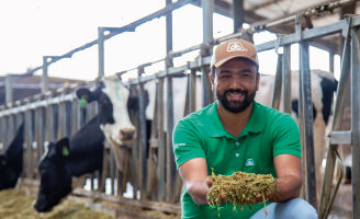 Homem de boné olhando para a câmera e segurando silagem nas mãos.