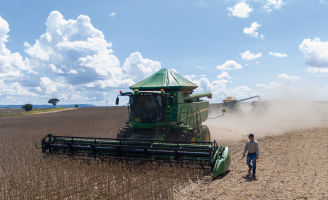 Colheitadeira fazendo a colheita de soja enquando um homem acompanha do lado.