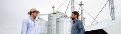 Dois homens conversando na frente de silos.