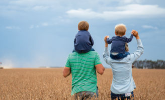 Homem e mulher de costas segurando seus filhos na garupa no meio da lavoura de soja.