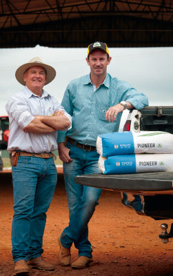 Dois homens olhando para a câmera ao lado de uma camionete com sacaria de soja dentro.
