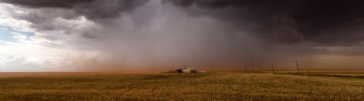 flat landscape with farmhouse in far distance under dark clouds