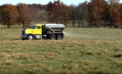 Truck applies impregnated fertilizer to field. 