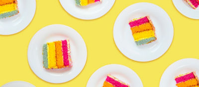Multiple plates with a piece of cake on each plate. The cake has a blue layer, yellow layer, orange layer and pink layer.