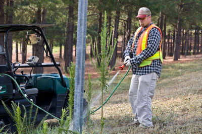 man spraying brush by pole with tank sprayer