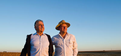 Dois homens um do lado do outro olhando para o horizonte, com céu azul no fundo.